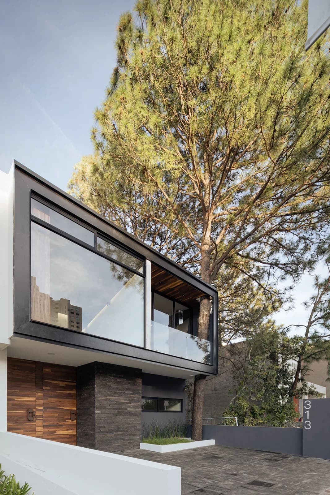 Fachada de Casa Dos Pinos con un voladizo acristalado entre dos pinos