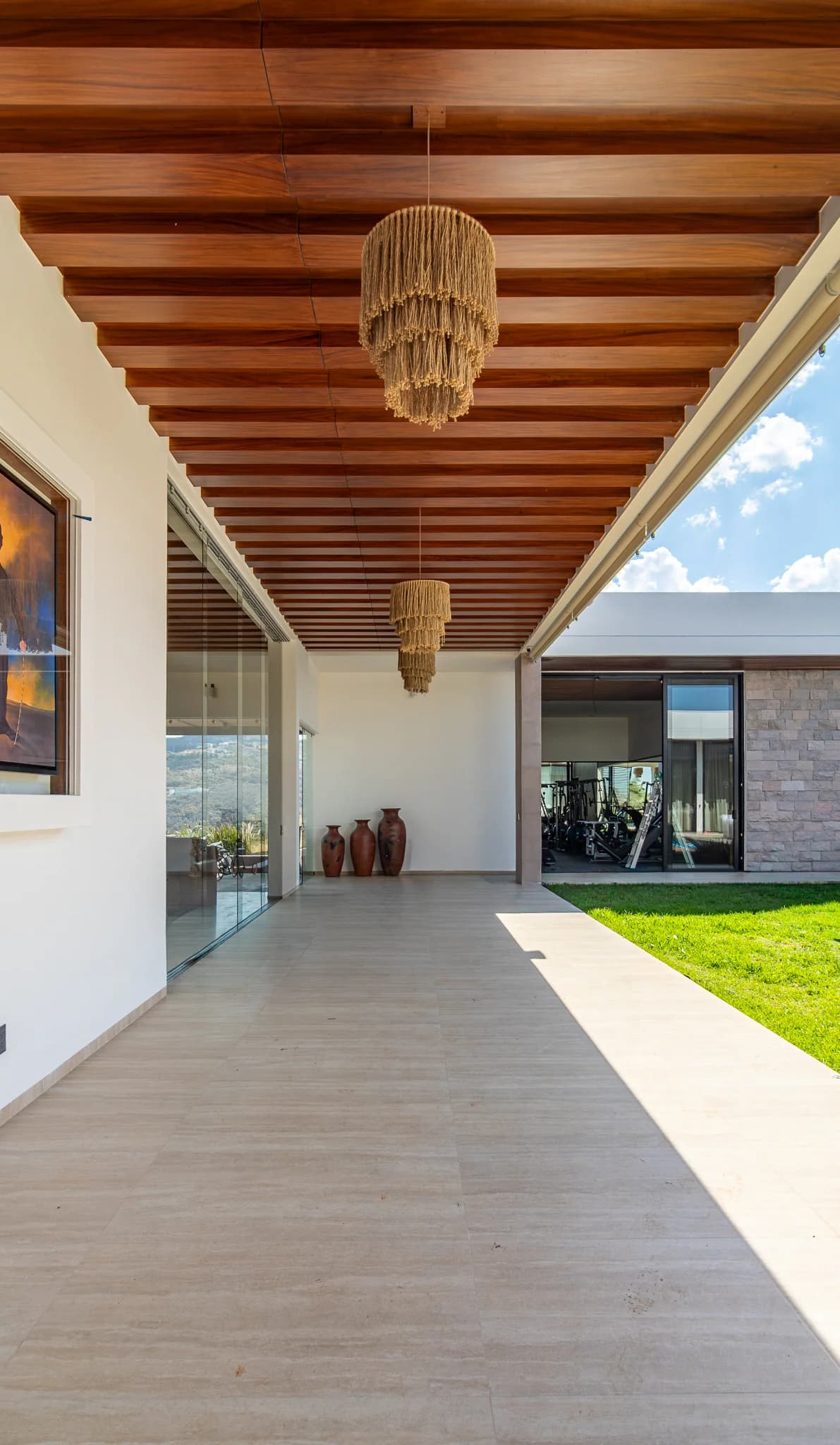 Pasillo de la casa L&C bajo un techo de vigas de madera, abierto al jardín al fondo