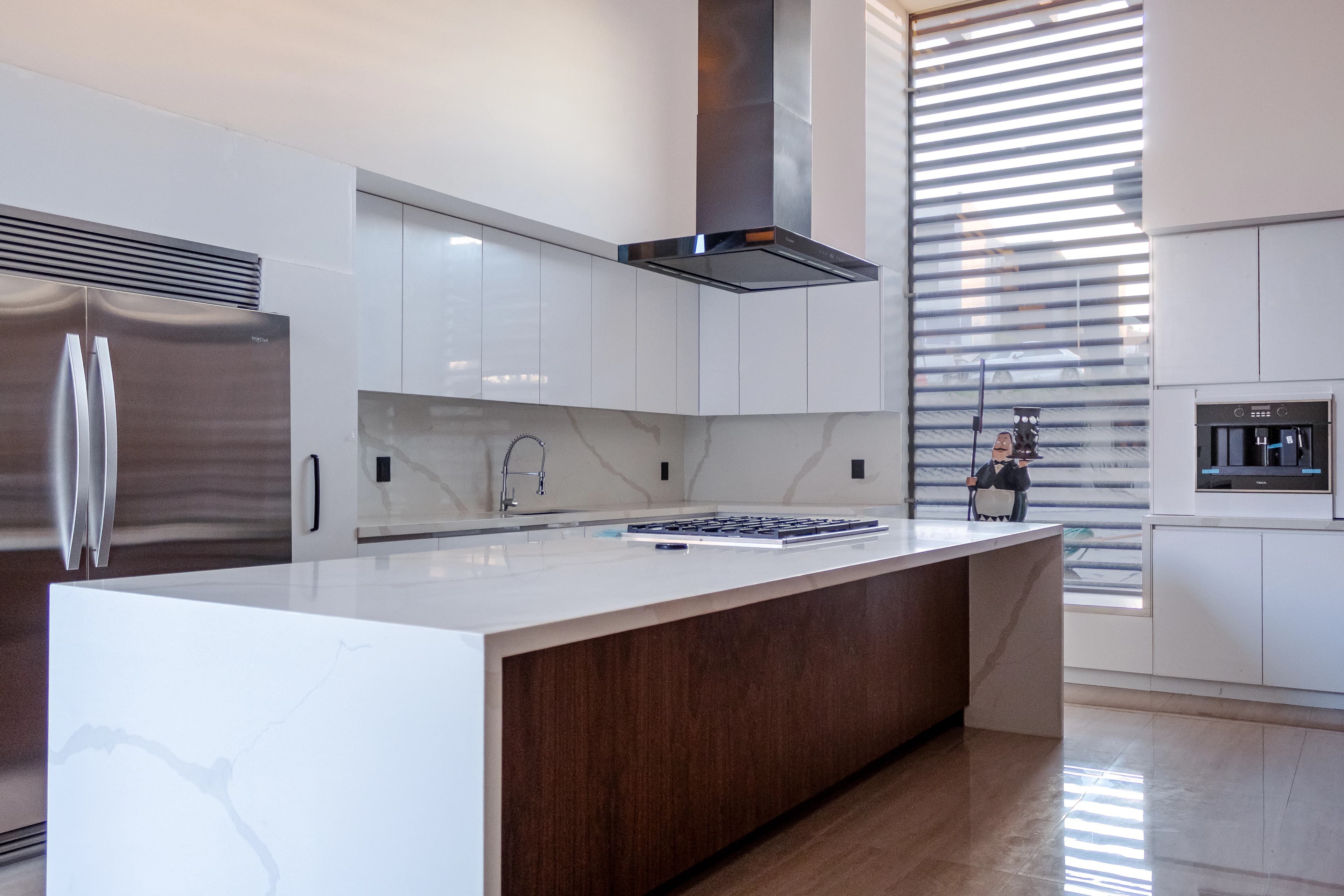 Cocina de L&C con isla de mármol blanco, frentes de madera y campana negra